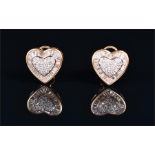 A pair of yellow metal and diamond heart-shaped earrings the central raised heart-shaped mount