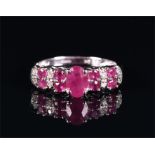 A 9ct white gold, diamond, and ruby ring centred with an oval-cut ruby, the shoulders with