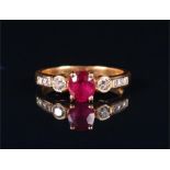 A 9ct yellow gold, diamond, and ruby ring set with an oval cut ruby, the shoulders inset with