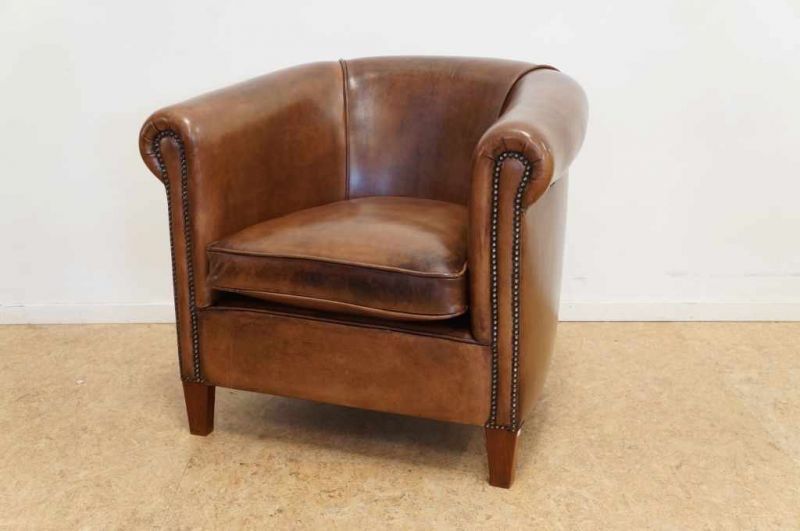 Engelse clubfauteuil geheel overtrokken met leer en rustend op houten poten An English leather