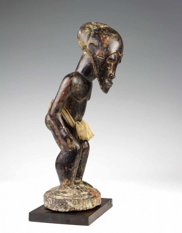 DRC., staand mannelijk figuur met gebogen lichaam, ovaal gelaat, ingekerfde kruizen op wangen,