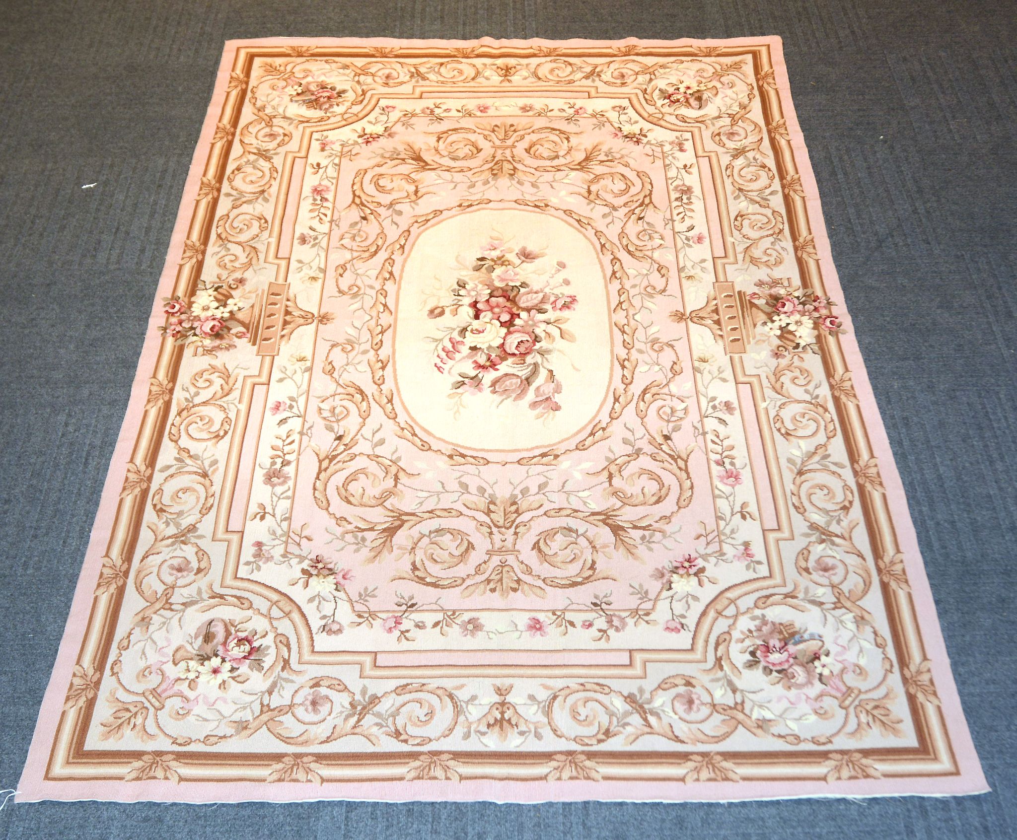 A modern rug in Aubusson style, woven in shades of pale pink, sepia, and cream
