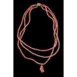 A three strand coral bead necklace, the three strands composed of uniform coral beads, suspending a