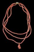 A three strand coral bead necklace, the three strands composed of uniform coral beads, suspending a