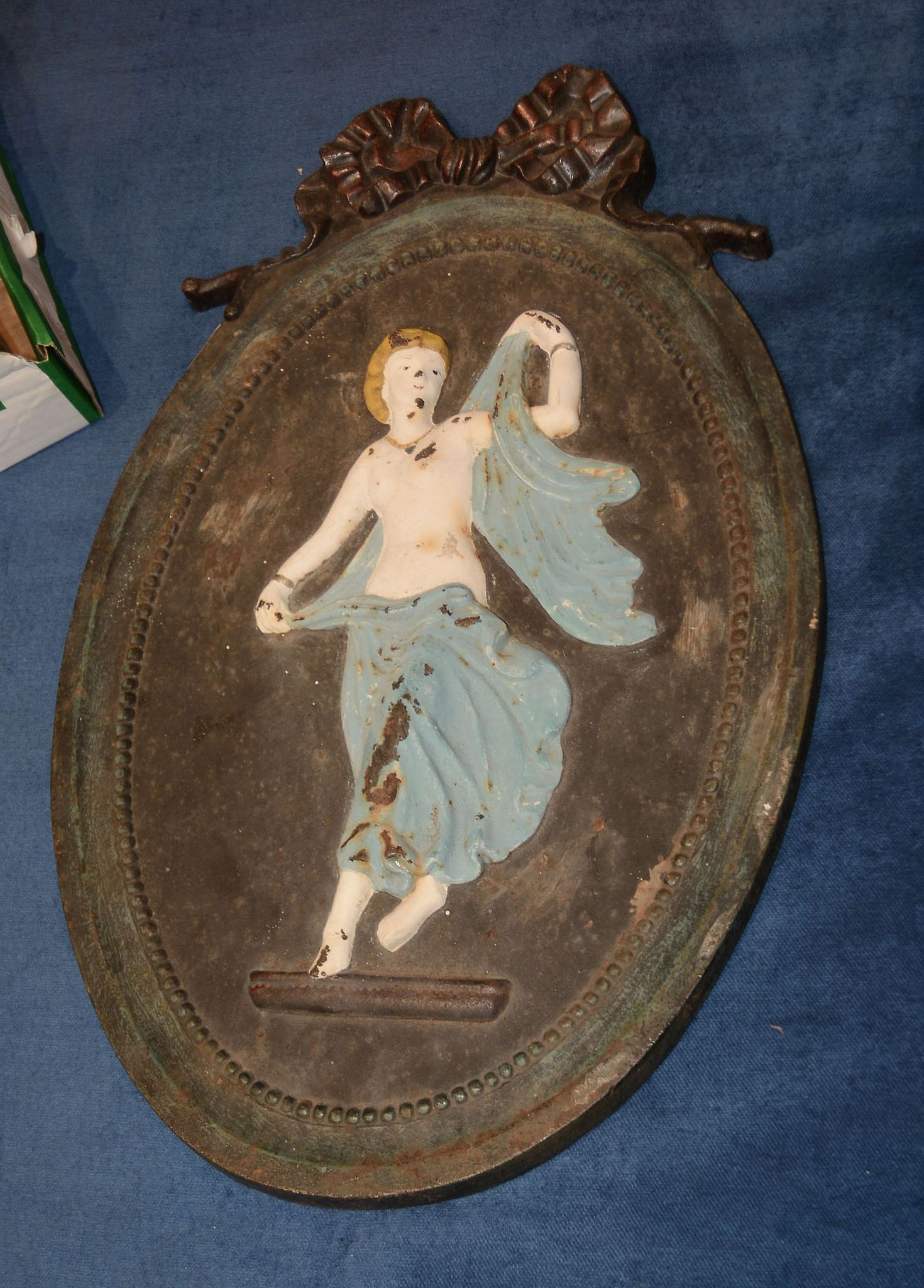 A cast iron wall plaque, cast in relief with dancing maiden and surmounted by a bow, 52cm x 32cm