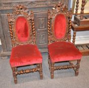 A pair of carved oak claret upholstered chairs in Carolean style,