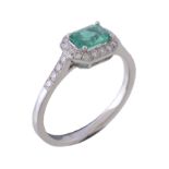 An emerald and diamond ring, the central rectangular cut emerald claw set within a surround of