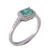 An emerald and diamond ring, the central rectangular cut emerald claw set within a surround of