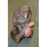 A Japanese Pottery Model of A Macaque, the simian sits cross-legged whilst holding a kinchaku and