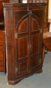 A George III oak corner wall cupboard, with pair of arched doors enclosing shaped shelves, 139cm