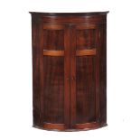 A George III mahogany hanging bowfront corner cupboard, circa 1780, the doors opening to a cream