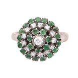 An emerald and diamond cluster ring in yellow gold, designed as a central round cut diamond