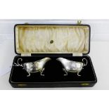 A cased pair of George V silver sauce boats with scroll handle and hoof feet by Elkington and Co,