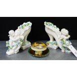 A pair of continental porcelain white glazed shoe figures surmounted by cherubs and floral garlands,