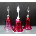 Three cranberry glass bells, one with a white handle, two with internal ringers, 28cm high (3)