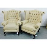 A pair of contemporary cream upholstered button back wing armchairs, raised on cabriole supports,