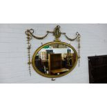A gilt framed oval wall mirror with egg and dart edge surmounted by swags of fruiting vines and an
