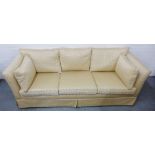 A cream upholstered three seater sofa with loose cushions, 70 x 210cm