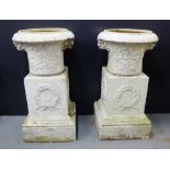 A pair of white painted garden planters with vine leaf pattern, each on a rectangular plinth base,