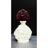 A white milk glass scent bottle with fruit and vine pattern in relief, complete with a red glass