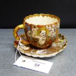 A Japanese Satsuma cup and saucer of lobbed form, painted with many faces and other motifs with
