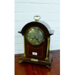 A mahogany and inlaid mantle clock, the arched top over a silver dial with Arabic numerals flanked