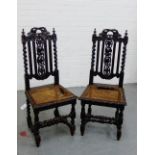 A pair of dark oak hall chairs with leaf carved top rail and splat back, flanked by barley twist