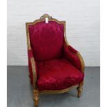 A giltwood framed armchair with red damask style upholstered back, arms and seat, raised on carved