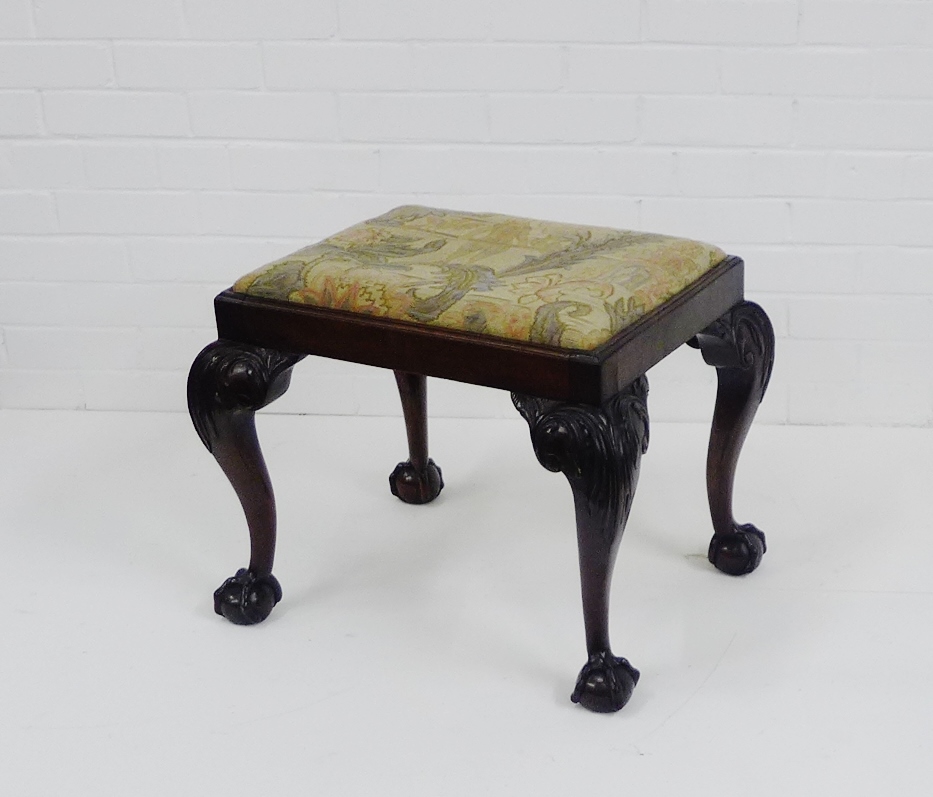 A 19th century mahogany stool. the floral upholstered top on carved leaf supports with claw and ball