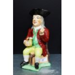 A Staffordshire Toby jug, modelled seated in black tricorn hat, brown coat and yellow breeches, with