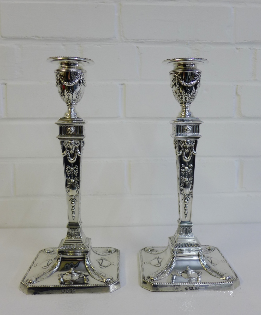 A pair of Edwardian silver candlesticks of neo-classical design, each with urn shaped tops above