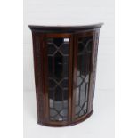 A wall hanging mahogany bow front corner cabinet, with dentil frieze over two astragal glazed doors,