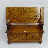 An oak monk's bench, with carved crested motif to back panel and floral panels to front, 65 x 110cm
