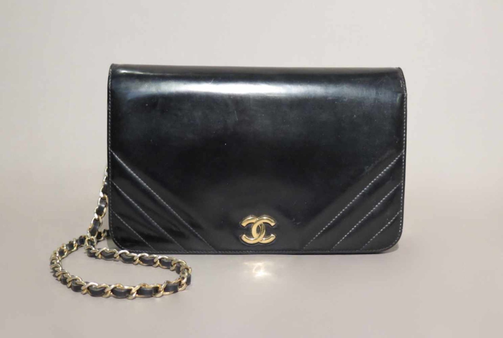 CHANEL.Sac.(haut. 15.5 cm, larg. 23.5 cm, prof. 5.5 cm). En cuir noir verni, garnitures en métal