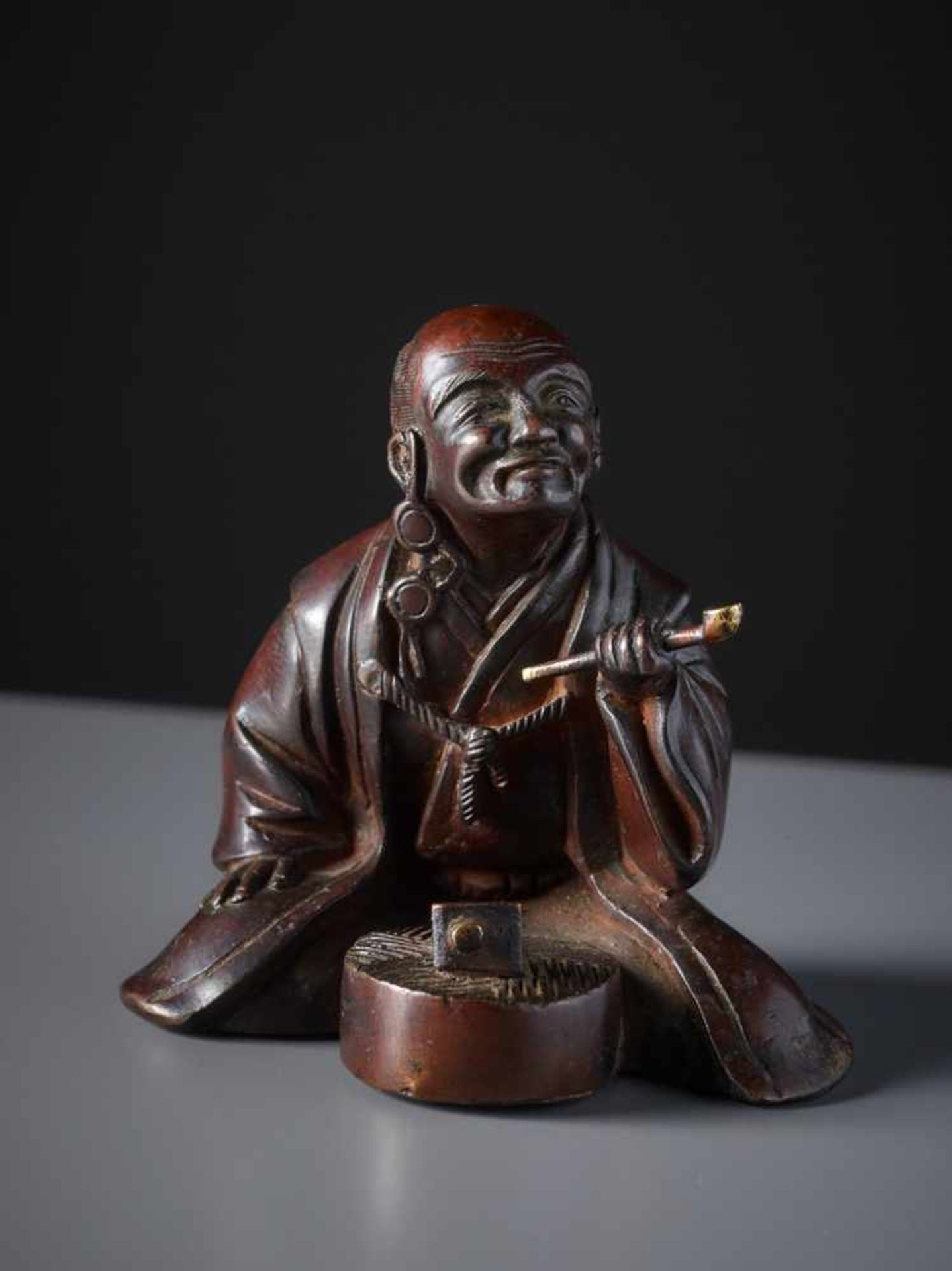 HANDWERKER MIT PFEIFE Gelbe Bronze, Japan. 19. Jh.Vor einem oben und unten flachen, kreisrunden