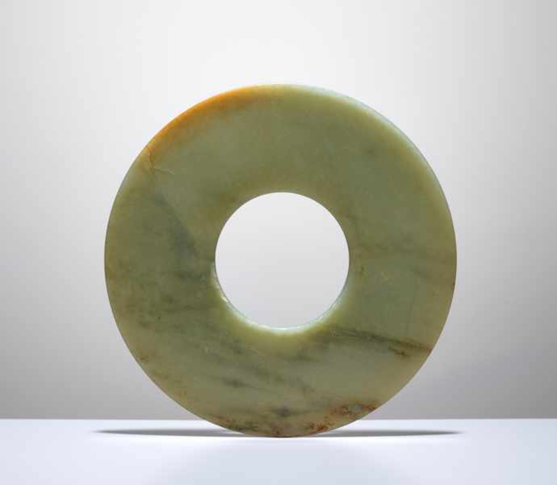 A SMOOTHLY POLISHED BI DISC WITH SHINY SURFACES CARVED FROM GREEN JADE WITH BROWN STRIPES Jade.