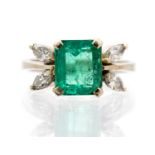 An emerald single stone white gold ring with diamond set leaf design shoulders,