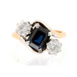 A blue stone and diamond three stone ring with cross over shoulders,