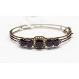 A Victorian amethyst and seed pearl rose metal bangle comprising centre claw set raised amethyst