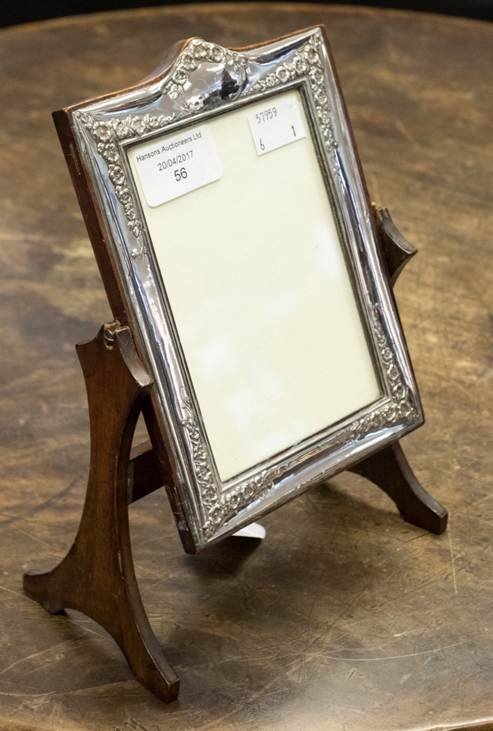 A silver picture frame on oak stand, the frame itself being embossed with floral pattern,