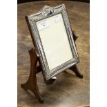 A silver picture frame on oak stand, the frame itself being embossed with floral pattern,
