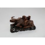 A Chinese carving of a recumbent water buffalo on hardwood stand with two handles