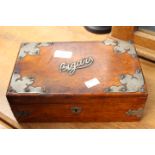 A wooden cigar box containing two silver spoons and a silver fork and assorted pencils,