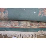 A large woollen rug, having a turquoise ground, with a panel of peach and cream floral decoration,