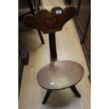 An oak tripod back-stool, the denticulated rail with carved heart motif,