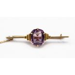 An Art Deco amethyst and gold bar brooch, claw set with a mixed cut rectangular amethyst,