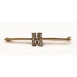 An Edwardian yellow metal bar brooch with a diamond set ' M ' with small old cut diamonds.
