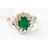 An emerald and diamond ring set with a central oval emerald with a diamond surround,