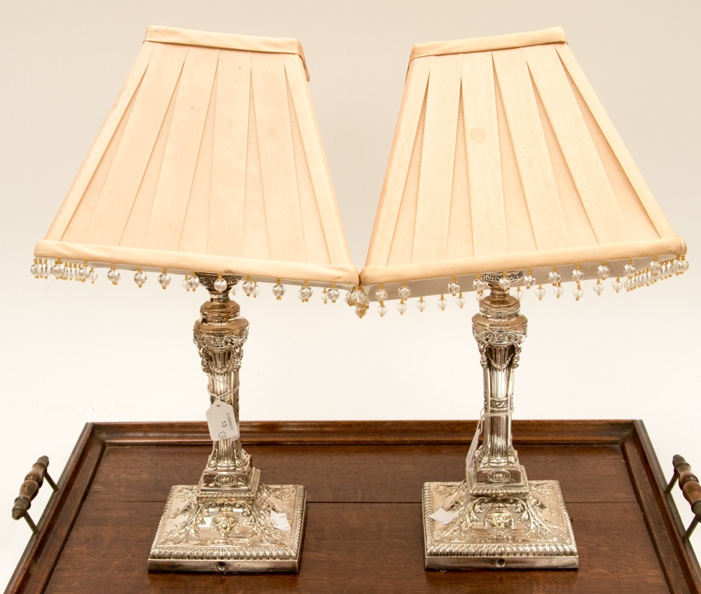 A pair of Silver plated lamps with square base forms embossed with foliate and urn details,