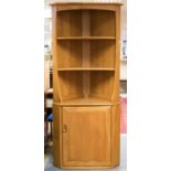 An Ercol Windsor light elm and ash corner cupboard, three open shelves over a single cupboard,